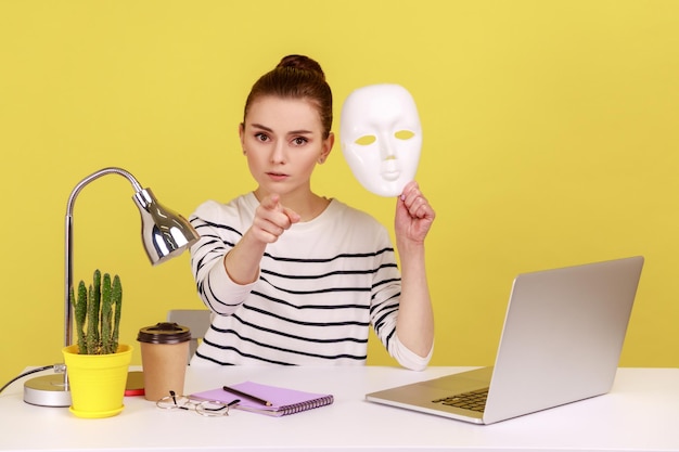 Lavoratrice con una maschera bianca e puntando il dito alla telecamera che ti accusa di nascondere l'identità