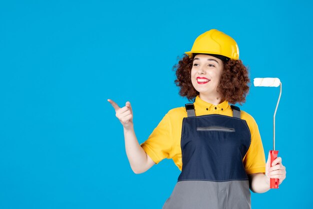 Lavoratrice in uniforme con rullo di vernice su un blu