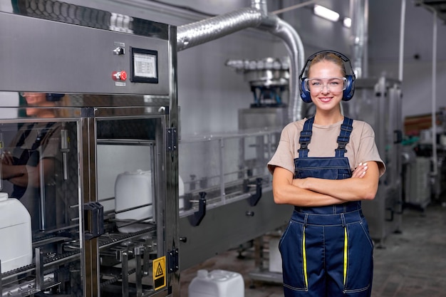 Lavoratrice in uniforme protettiva che lavora nella ricerca di forniture mediche e nella fabbrica di produzione di pesticidi, la donna sta controllando la produzione di contenitori per bottiglie prima della spedizione. Capannone industriale.