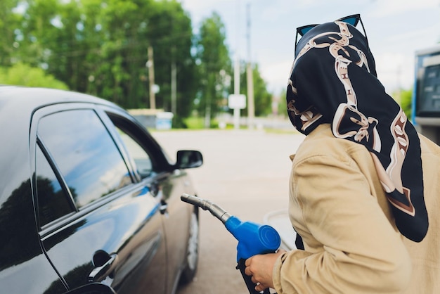 Lavoratrice musulmana tailandese che indossa l'hijab riempie il carburante per un'auto con una pistola a benzina alla stazione di servizio