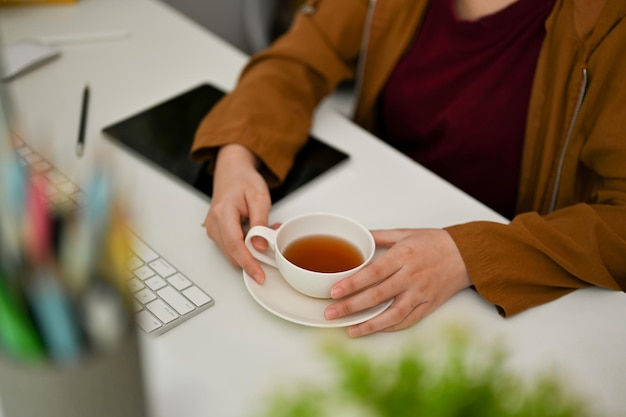 Lavoratrice o graphic designer seduto alla sua scrivania in ufficio con un tè pomeridiano in ufficio