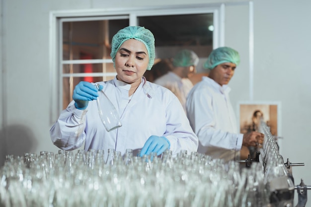 Lavoratrice senior che pulisce e controlla le bottiglie di vetro sporche per le bevande a base di succo nella fabbrica di bevande