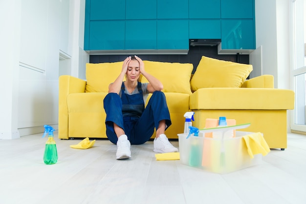 Lavoratrice stanca del servizio di pulizia che si siede vicino allo strato e che ritiene triste dopo avere lavato pavimento su cucina.