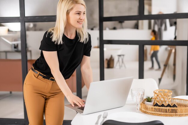 Lavoro a distanza a casa, freelance durante la quarantena covid-19. Signora sorridente che si siede e che lavora al computer portatile nell'interno accogliente del salone, spazio libero.