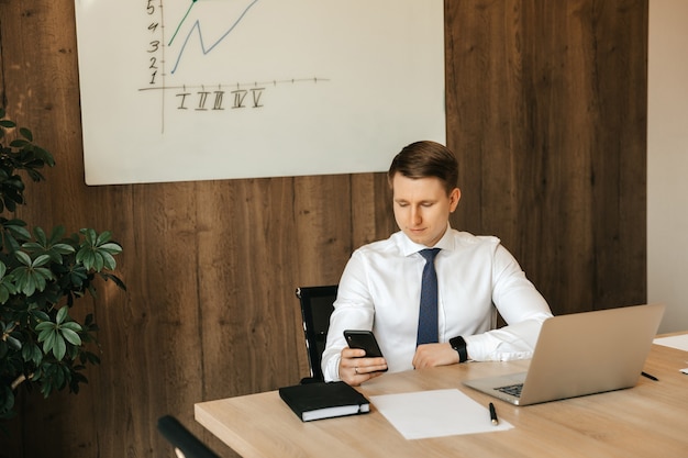 Lavoro a distanza al computer. Distratto dal lavoro, un uomo guarda il social network su uno smartphone.