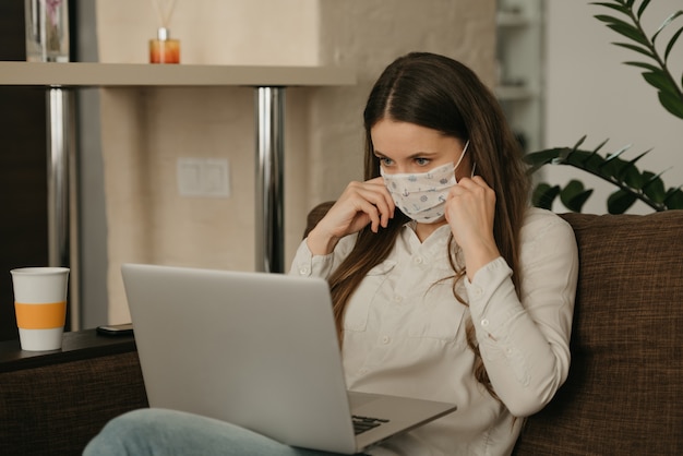 Lavoro a distanza. Donna in una mascherina medica che studia a distanza sul suo computer portatile durante la quarantena