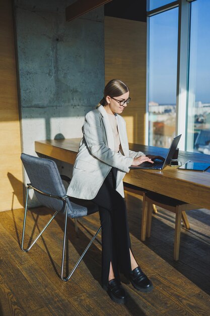 Lavoro d'ufficio attraente giovane manager femminile che lavora in ufficio in piedi in un'area di lavoro luminosa utilizzando un moderno computer portatile ragazza che ha una videochiamata tramite laptop