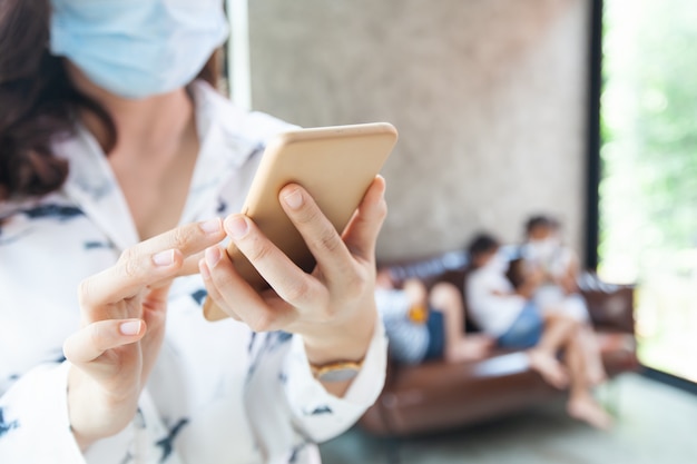 Lavoro da casa Donna in quarantena per Coronavirus COVID-19 che indossa una maschera protettiva usando su smartphone e lavora a casa mentre i suoi figli giocano a casa durante l'epidemia di coronavirus