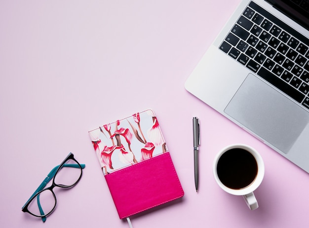 Lavoro da casa. Piatto business giaceva con una tazza di caffè, nota, matita, occhiali da vista, notebook su sfondo rosa