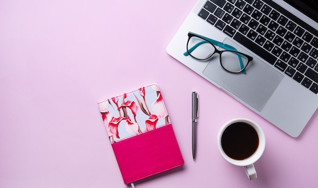 Lavoro da casa. Piatto business giaceva con una tazza di caffè, notebook, occhiali, matita su sfondo rosa