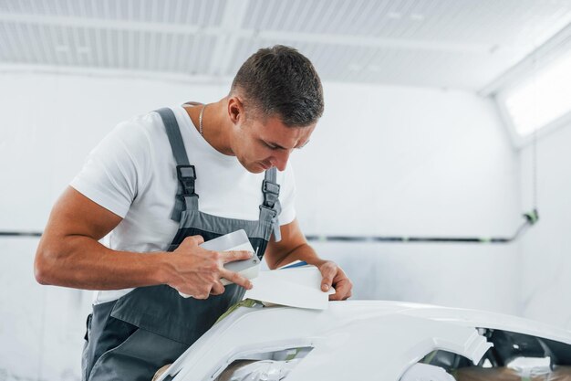 Lavoro dettagliato Il riparatore di automobili caucasico in uniforme ha un lavoro in garage