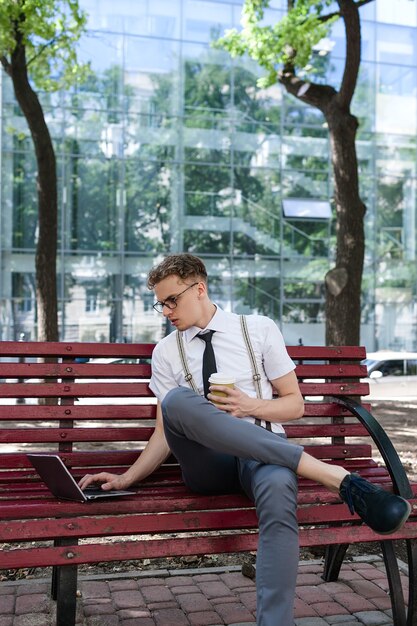 Lavoro eccessivo. Scadenza. stile di vita aziendale. uomo che tiene una tazza di caffè seduto in un parco urbano con un laptop su una panchina