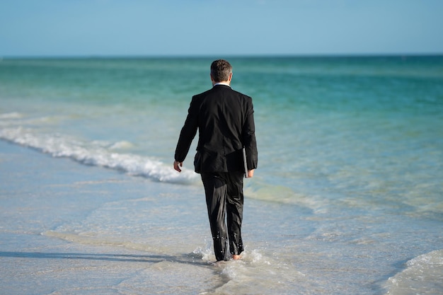 Lavoro freelance business online affari estivi vista posteriore dell'uomo d'affari posteriore in tuta in acqua di mare a