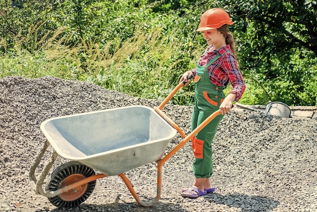 Lavoro minorile allegro che usa l'uniforme da costruzione e la carriera futura della carriola da costruzione