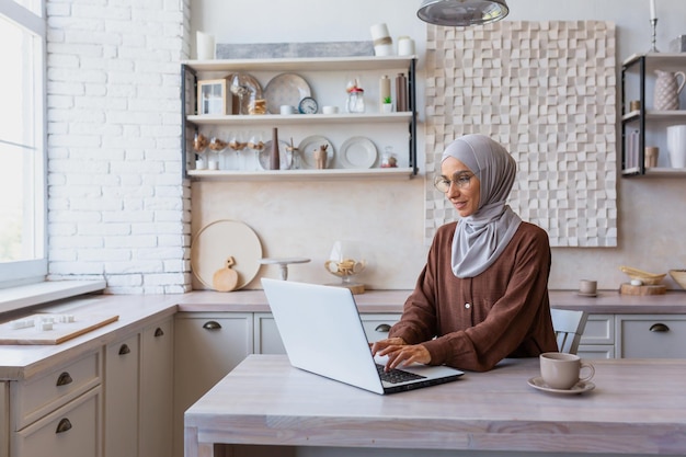 Lavoro online da casa una giovane donna musulmana in hijab siede a casa in cucina al tavolo e