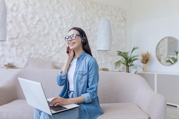 Lavoro online giovane bella donna freelance in occhiali e jeans seduto a casa sul divano e