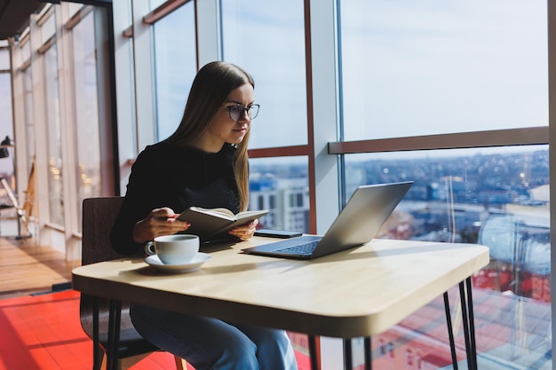 Lavoro online in un bar Ragazza felice in abiti casual e occhiali che utilizza un laptop Lavoro o istruzione a distanza con le moderne tecnologie digitali per uno stile di vita confortevole in città