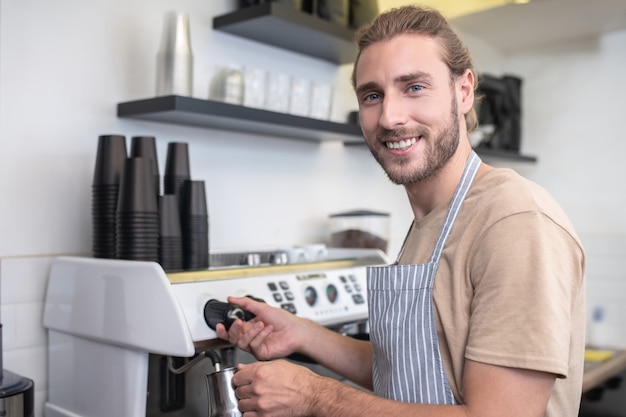 Lavoro preferito. Occupato felice giovane barbuto versando acqua per il caffè mentre si trova nel suo caffè