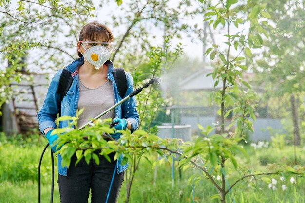 Lavoro primaverile estivo in giardino donna con zaino pistola a spruzzo da giardino sotto pressione che maneggia alberi da frutto di peri affetti da malattie batteriche Protezione e cura delle piante dagli insetti nocivi