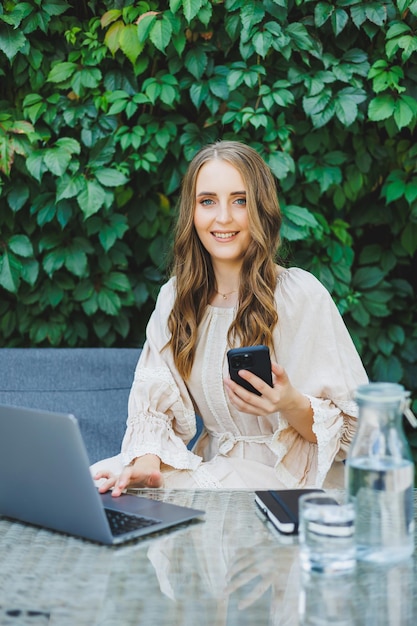 Lavoro remoto di una donna freelance su una terrazza estiva su un laptop Una donna d'affari in abito beve acqua e lavora su un laptop