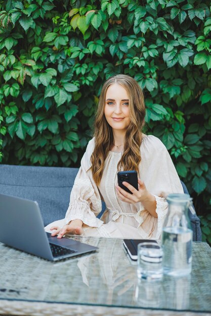 Lavoro remoto di una donna freelance su una terrazza estiva su un laptop Una donna d'affari in abito beve acqua e lavora su un laptop