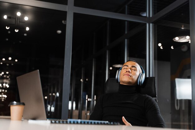 Lavoro straordinario L'uomo asiatico con gli occhi chiusi sta riposando al lavoro al computer portatile Programmatore maschio stanco che si prende una pausa a causa del lavoro straordinario