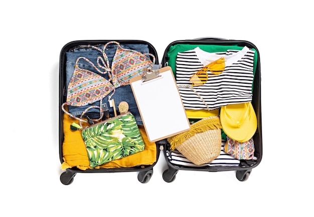 Lay piatto con valigia aperta con abiti casual per le vacanze estive sul muro bianco. Vacanze estive, viaggi, turismo, concetto di bagaglio di volo. Vista dall'alto