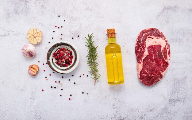 Lay piatto di bistecca di manzo crudo fresco con rosmarino e spezie su sfondo bianco squallido cemento vista dall'alto