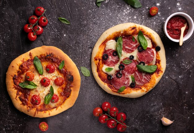 Lay piatto di due pizze con pomodori e basilico sulla tavola nera