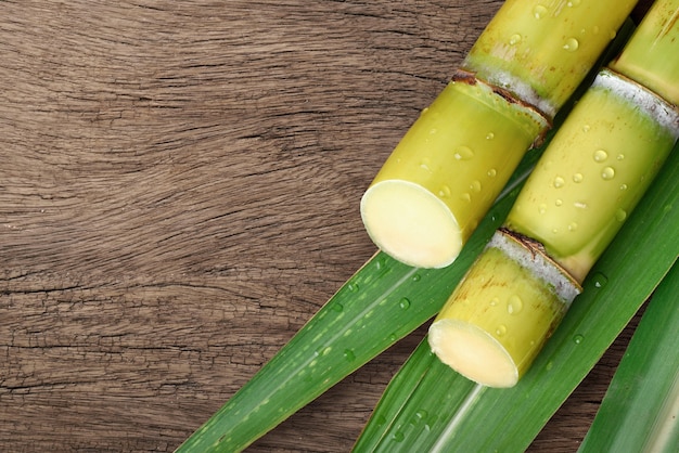 Lay piatto (vista dall'alto) di canna da zucchero fresca con goccioline d'acqua su uno sfondo di legno.