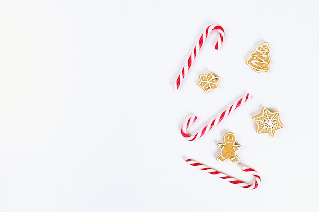 Layout di Natale. Caramelle di canna rosso-bianco a strisce e biscotti di zenzero fatti in casa su uno sfondo bianco