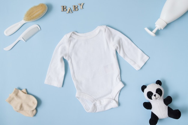 Layout piatto di abbigliamento per bambini. di un body bianco per bebè su una superficie blu