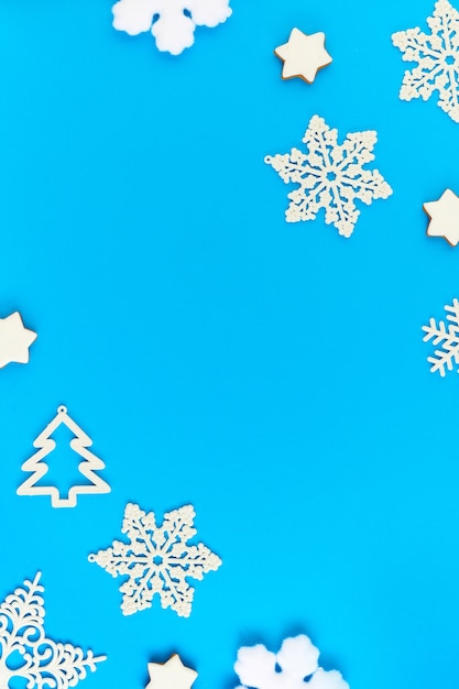 Layout piatto di fiocchi di neve decorativi bianchi e abeti che circondano copyspace per i tuoi saluti, testo pubblicitario o messaggio su sfondo blu