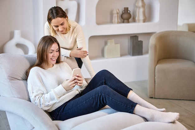 Le amiche allegre chiacchierano in messenger nel telefono al chiuso