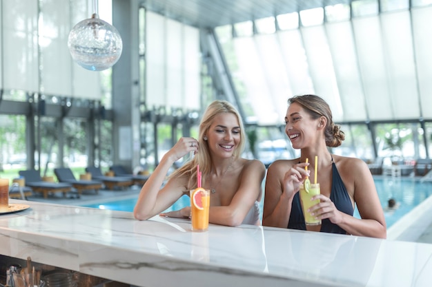 Le amiche bevono cocktail mojito al bar della piscina indossano bikini hotel di lusso vicino alla piscina