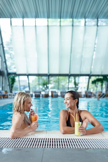 Le amiche delle donne bevono un cocktail mojito sul bar della piscina indossano un bikini hotel di lusso vicino alla spiaggia sull'isola tropicale rilassano Belle giovani donne che si divertono in piscina a bere un cocktail sorridente