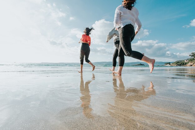 Le amiche felici corrono sulla spiaggia del mare durante una giornata luminosa, gli amici si rilassano felici divertendosi giocando sulla spiaggia vicino al mare quando il tramonto la sera