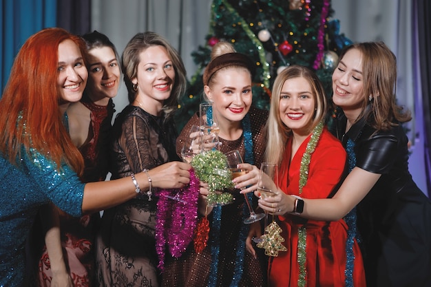 Le amiche festeggiano il Natale e il Capodanno vicino all'albero di Natale. Le donne brindano con champagne, ridono e si rallegrano.