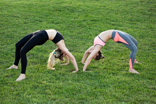 Le amiche praticano yoga nel parco sull'erba