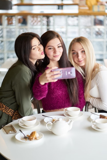 Le amiche si divertono nel caffè, bevono tè e fanno selfie