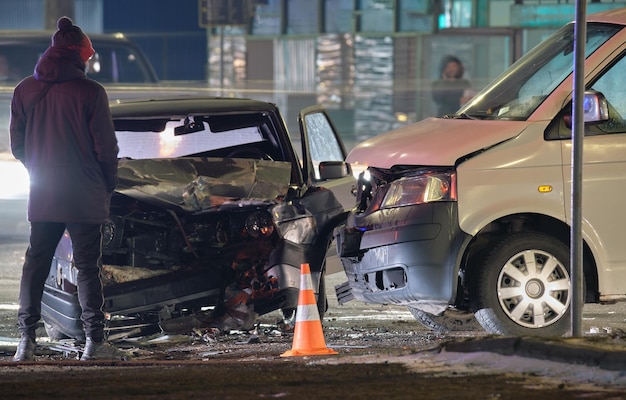 Le auto si sono schiantate pesantemente in un incidente stradale dopo la collisione e la silhouette di persone sulla strada della città di notte Concetto di sicurezza e assicurazione stradale