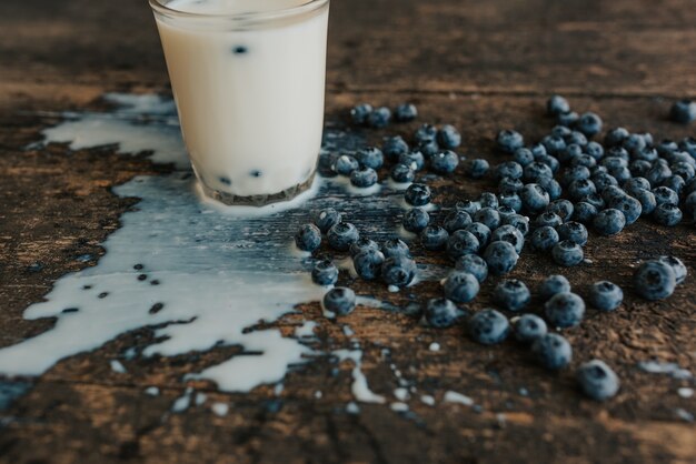 le bacche vengono lanciate in vetro trasparente facendo schizzi di latte. mirtilli freschi blu sparsi