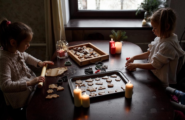 Le bambine carine stanno cucinando il pan di zenzero di Natale su un tavolo di legno Preparazione del passatempo familiare per le vacanze di Natale