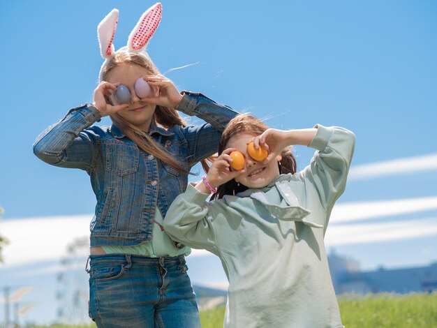 Le bambine con le orecchie di coniglio tengono le uova colorate di Pasqua vicino ai loro occhi su uno sfondo di cielo blu