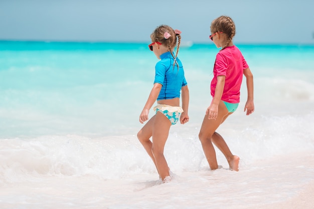 Le bambine divertenti felici si divertono molto in spiaggia tropicale giocando insieme.