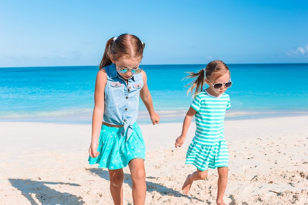 Le bambine divertenti felici si divertono molto in spiaggia tropicale giocando insieme.