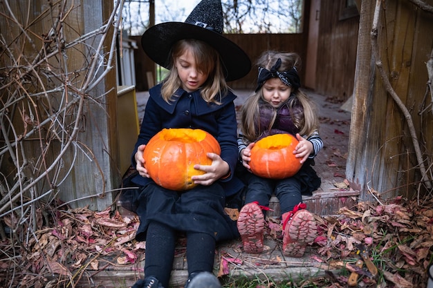 Le bambine fanno jackolantern da grandi zucche per la celebrazione delle vacanze di Halloween Cappotto da cappello da strega Tagliare con il coltello togliere la polpa con i semi Attività all'aperto nel cortile Festa per bambini