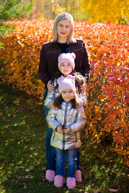 Le bambine in abiti identici con la madre si divertono a passeggiare nel parco in autunno