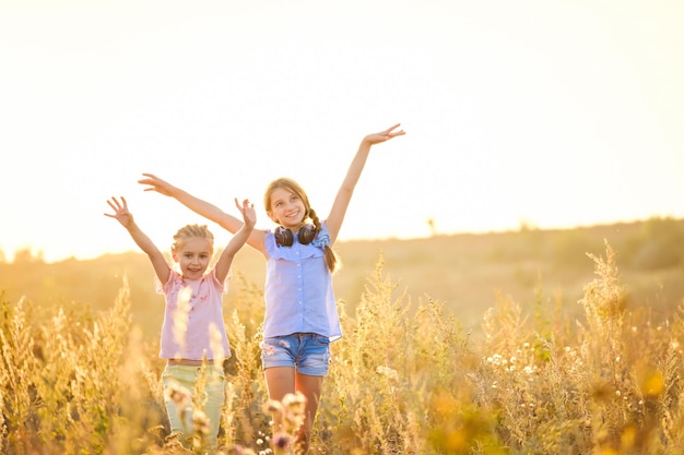 Le bambine sorridenti stanno in piedi sul campo serale del sole con le mani alzate con gioia