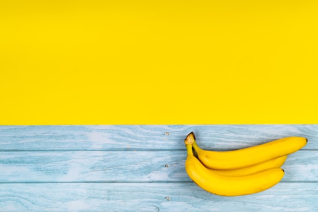 Le banane gialle giacciono su uno sfondo di legno blu e uno sfondo giallo.